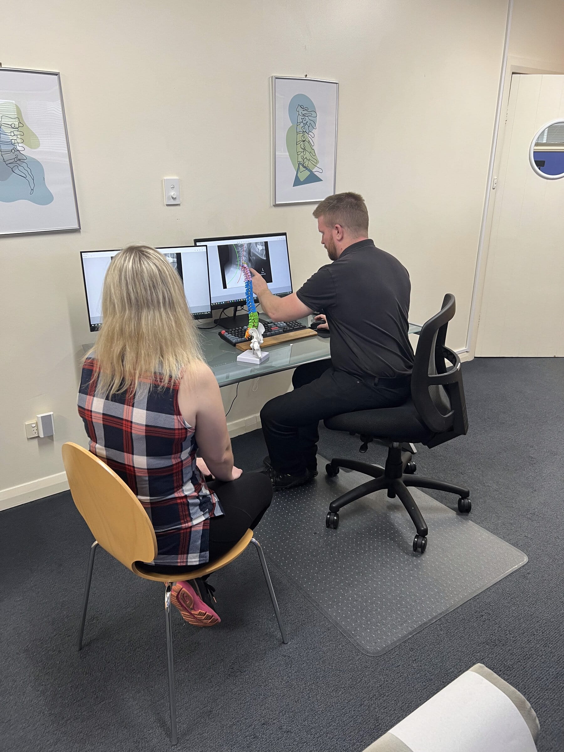Chiropractor reviewing X-ray results with patient on dual monitors at Stapleton Chiropractic